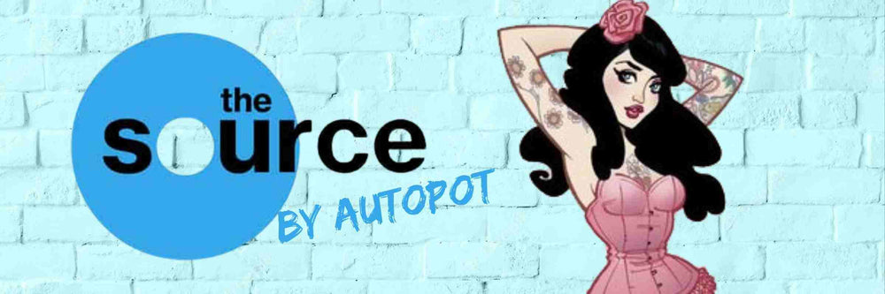 SEXY TATTOOED PINUP GIRL IN A PINK CORSET WITH A PINK ROSE IN HER BLACK HAIR, STANDING NEXT TO THE SOURCE BY AUTOPOT LOGO ON A BLUE BRICK WALL BACKGROUND